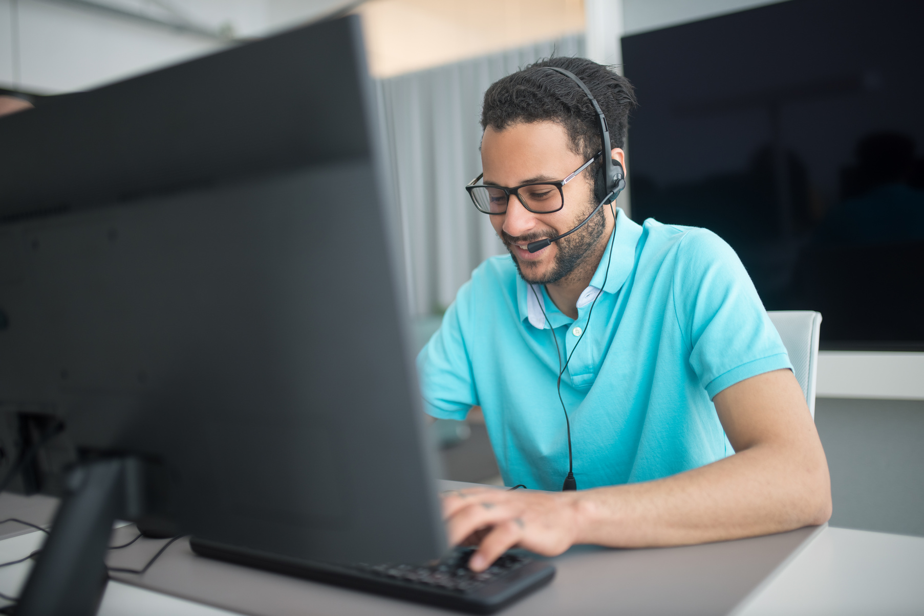 Man in Blue Polo Shirt with Headset Using Black Computer